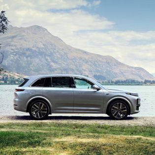A silver SUV parked by a lake with mountains in the background.