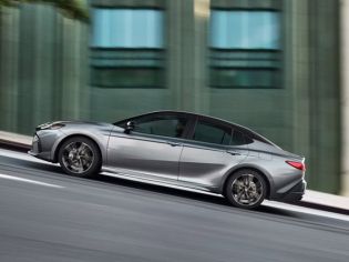 Side profile shot of sleek silver sport sedan driving on urban road, showcasing sculpted body lines, alloy wheels and modern fastback rear styling