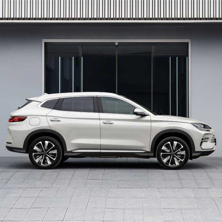 A white SUV with a sleek side profile, featuring stylish alloy wheels and a streamlined body, parked in front of a modern building with large glass windows.