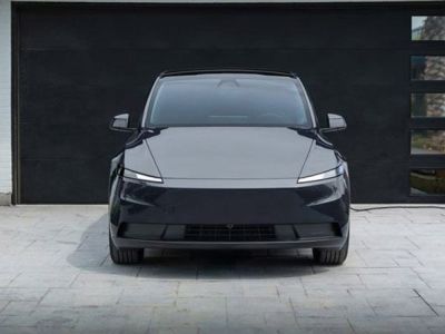 Front view of a sleek black electric SUV parked in a driveway, connected to a home charging station, with a modern garage and landscaped area, embodying eco-friendly and minimalist design.