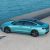 A teal sedan parked by the sea.