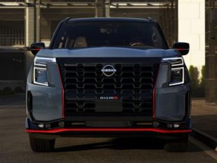 Front view of a bold Nissan pickup truck, featuring a large black V-motion grille, angular LED headlights, and striking red accent trim.
