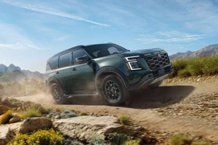 2026 Nissan Armada NISMO driving on a dirt road near some rocks and wildflowers