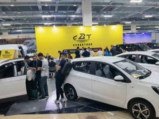 A car exhibition scene with several white cars on display, a large yellow "CBT CYBERTRON" backdrop, and people interacting, set in an indoor exhibition hall.