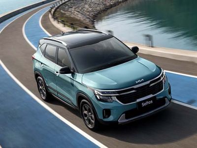 A blue Kia Seltos SUV driving on a curved road by the water.