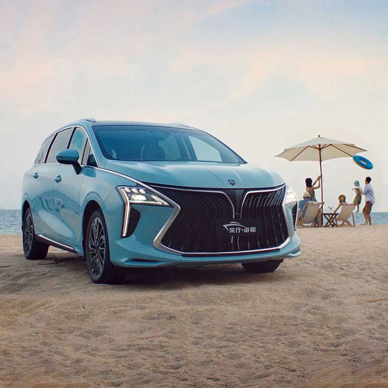 A light blue MPV is parked on a sandy beach, with the sea and a family enjoying the shore in the background, highlighting its stylish design and family-friendly appeal.