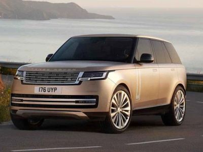 A beige Range Rover with license plate 176 UYP, parked on a coastal road with a scenic sea and mountain backdrop, showcasing luxury and adventure.