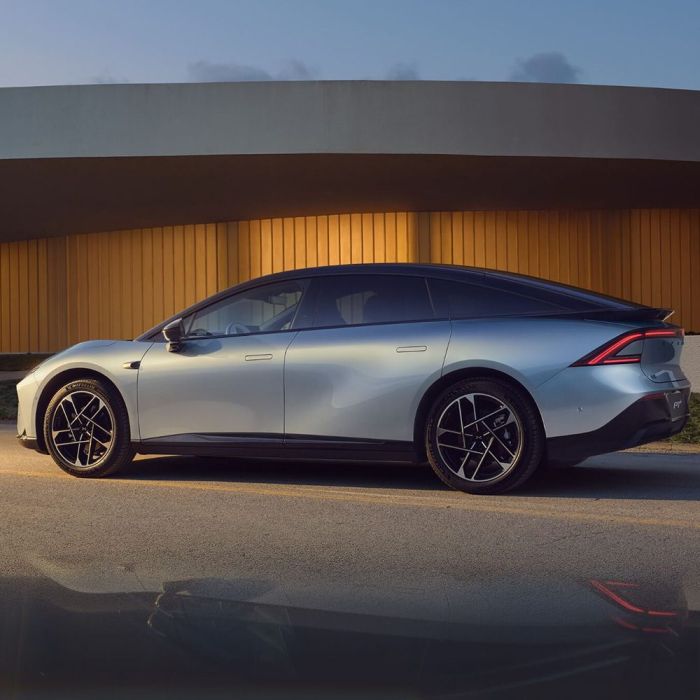 Side view of a silver electric car parked in front of a modern building with a golden facade.