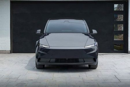 Front view of a sleek black electric SUV parked in a driveway, connected to a home charging station, with a modern garage and landscaped area, embodying eco-friendly and minimalist design.