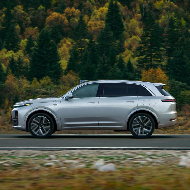 A silver SUV driving on a road with a forest in the background.