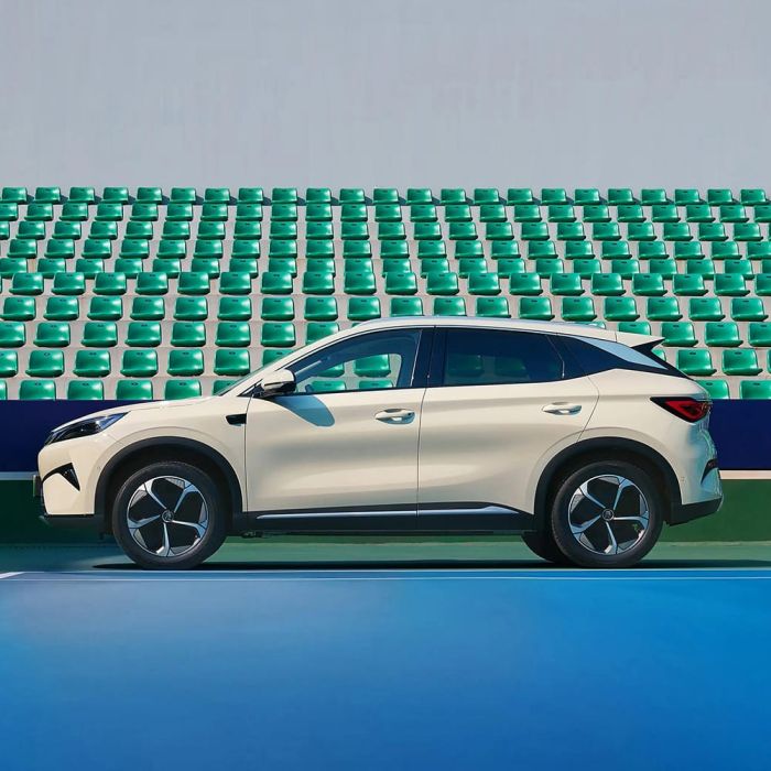 A light - colored BYD Yuan Plus electric SUV parked on a tennis court with green seats in the background.