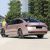 Rear side view of a pink Volkswagen Passat sedan parked on a road, with trees and a building in the background.