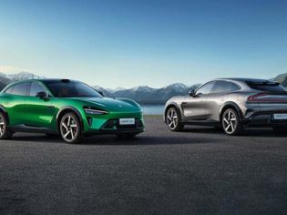 Two Xiaomi electric cars, one green and one silver, parked on a paved area with a scenic backdrop of mountains and a lake.