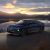 A dark blue NIO ET9 electric car driving by a lake at sunset with mountains in the background.