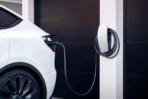 White electric vehicle charging at a sleek, wall-mounted home charging station next to a dark garage door.