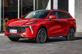 A red Forthing T5 EVO SUV with a black roof, showcasing its bold grille and sleek design, parked on a paved area in front of a modern building with large glass windows.