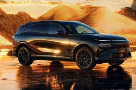 Xpeng G9 parked on reflective wet ground, set against a glowing golden desert landscape at sunset.