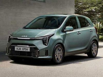 A light green Kia car with the license plate "KJA 0704" parked beside a gray building in a sunny outdoor setting.