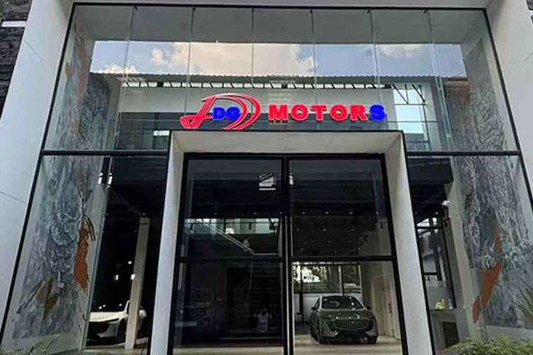 Exterior of "DG Motors" car dealership with glass facade and cars displayed inside.