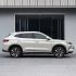 A white SUV with a sleek side profile, featuring stylish alloy wheels and a streamlined body, parked in front of a modern building with large glass windows.