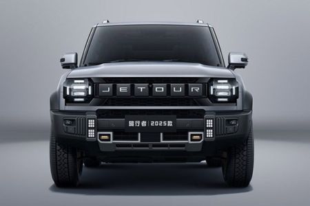 The 2025 Jetour Traveler SUV, in a sleek gray finish, features a bold front design with prominent "JETOUR" branding and rugged off-road elements, showcased against a minimalist gray backdrop.