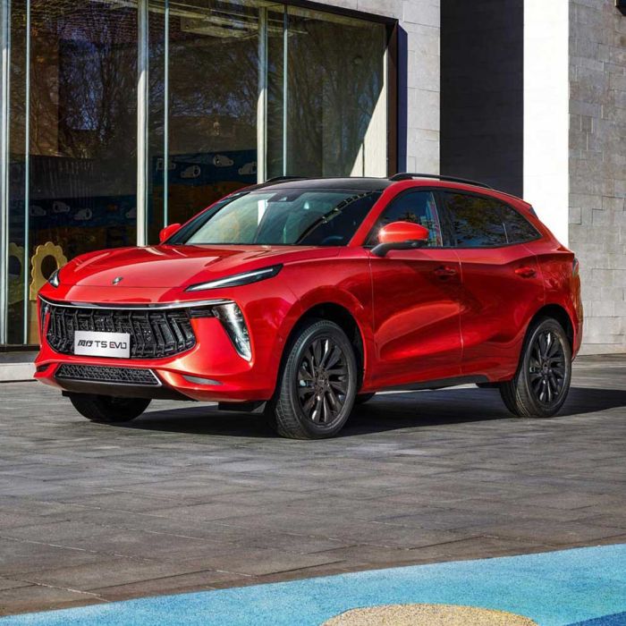 A red Forthing T5 EVO SUV with a black roof, showcasing its bold grille and sleek design, parked on a paved area in front of a modern building with large glass windows.