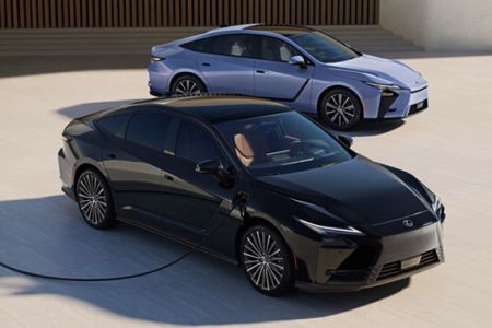 Two sleek modern electric sedans in black and light blue parked outdoors; front vehicle plugged in for charging against neutral backdrop