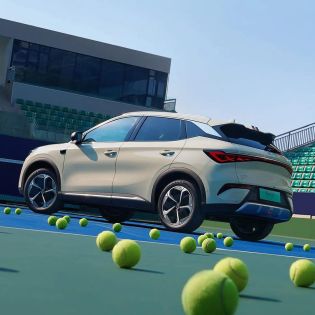 A light - colored BYD Yuan Plus electric SUV on a tennis court with tennis balls around.
