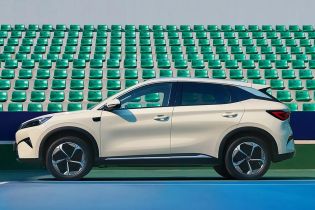 A light - colored BYD Yuan Plus electric SUV parked on a tennis court with green seats in the background.