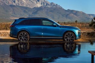 A blue Xpeng electric SUV parked by a reflective body of water, with a majestic mountain range in the background.