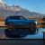 A blue Xpeng electric SUV parked by a reflective body of water, with a majestic mountain range in the background.