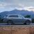 A gray SUV driving on a road with mountains in the background.