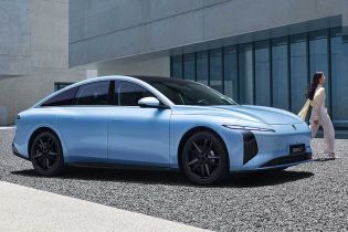 A light blue electric sedan, Xinghai S7, with a sleek design and black wheels, parked near a modern concrete building, with a woman in light clothing walking beside it.