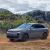 A gray Li Auto L7 driving on a dirt road with mountains and trees in the background.