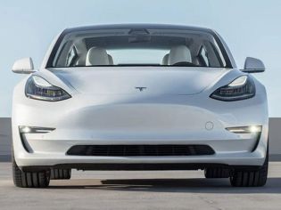 Front view of a white Tesla Model 3 sedan, featuring sleek headlights, a minimalist front design, and a spacious interior, parked on a concrete surface under a clear sky.