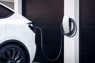 White electric vehicle charging at a sleek, wall-mounted home charging station next to a dark garage door.