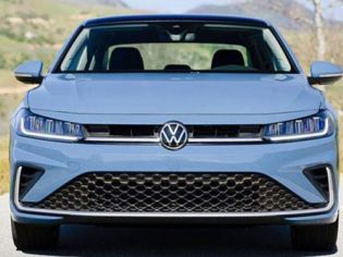 Front view of light blue Volkswagen car: iconic VW logo, sleek LED headlights, grille, on road with green hills.