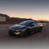 A dark gray Xpeng P7+ electric car driving on a road with mountains and a sunset sky in the background.
