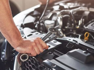 Mechanic's hand using a wrench to work on a car engine, performing maintenance, repair, or diagnostic service in an auto shop.