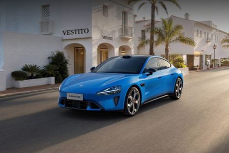 A bright blue Xiaomi SU7 sports sedan parked on a Mediterranean-style street with palm trees.
