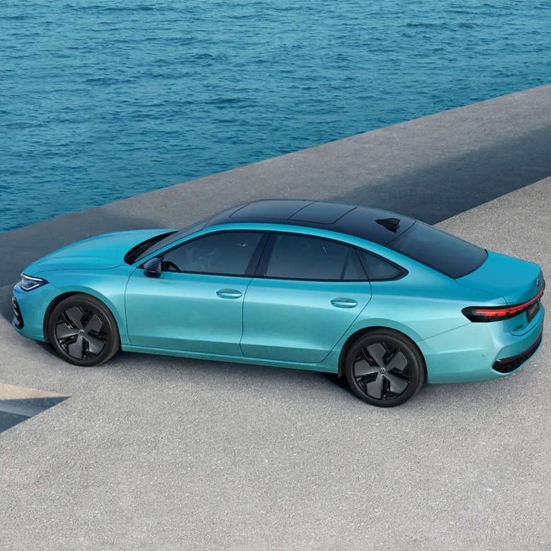 A teal sedan parked by the sea.