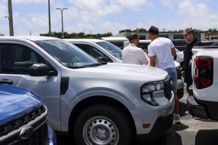 Ford Maverick pickup trucks: A group of people inspecting white Ford Mavericks at an outdoor car dealership lot.