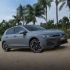 A gray Volkswagen Golf parked on sandy ground with palm trees in the background.