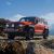 An orange off - road SUV parked on a rocky mountain terrain under a blue sky with white clouds.