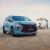 A light blue MPV is parked on a sandy beach, with the sea and a family enjoying the shore in the background, highlighting its stylish design and family-friendly appeal.