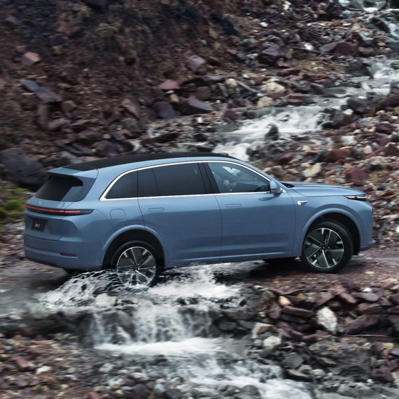 A light blue SUV driving through a stream in a rocky, mountainous area.