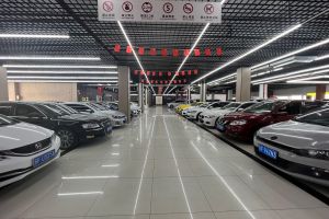A neatly arranged car showroom with various cars parked in rows, safety signs hanging from the ceiling, and red flags decorating the space.