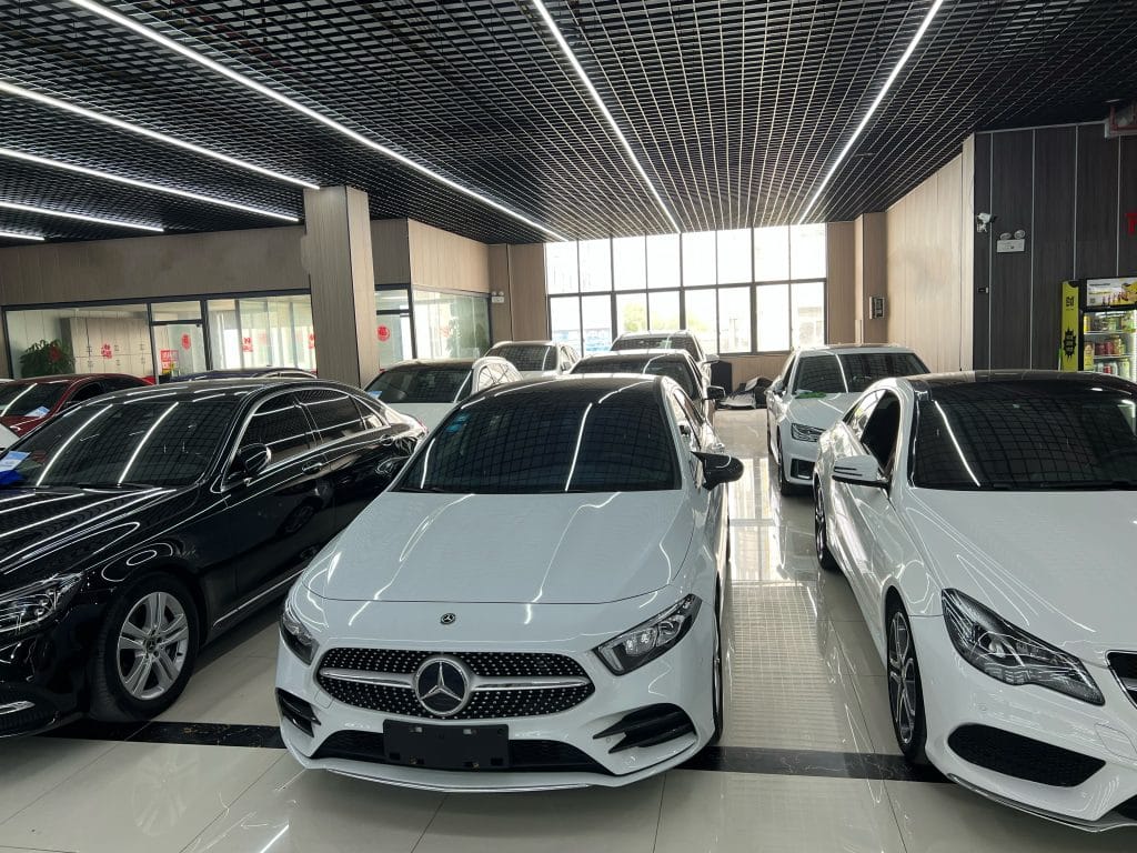 Plusieurs voitures, dont une Mercedes-Benz blanche, exposées dans une salle d'exposition bien éclairée.