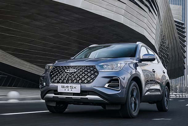 A Chery Tiggo 5x is driving on the road in front of a modern building.