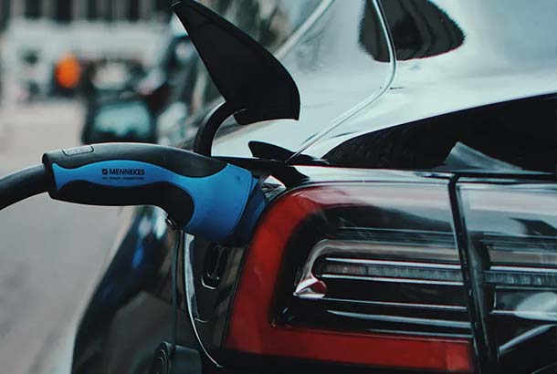 Close - up of an electric car being charged with a blue charging plug.